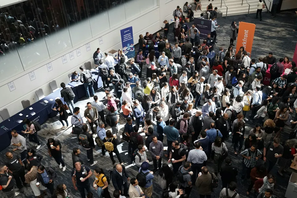Crowded indoor networking event with company booths and banners