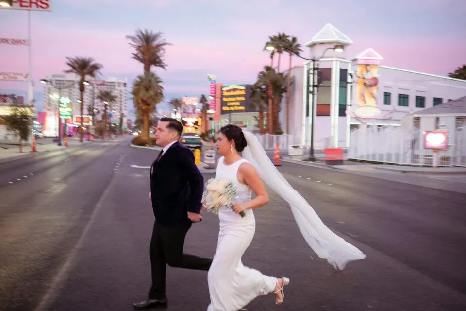 Bride and groom running hand-in-hand across a Las Vegas street at dusk
