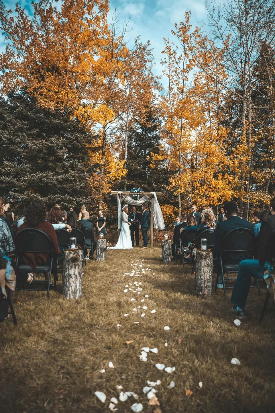 Outdoor autumn wedding ceremony under a wooden archway in a forest clearing